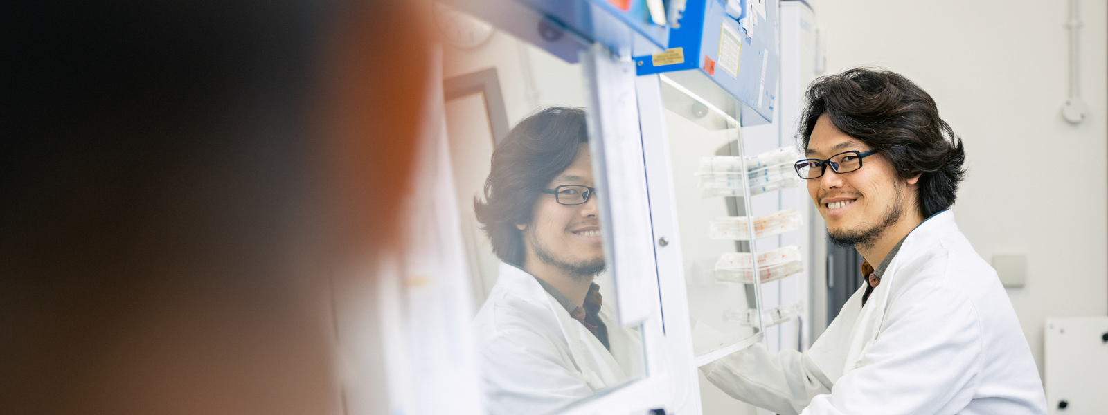 Researcher working in a tissue and cell culture room looks towards a colleague in the foreground